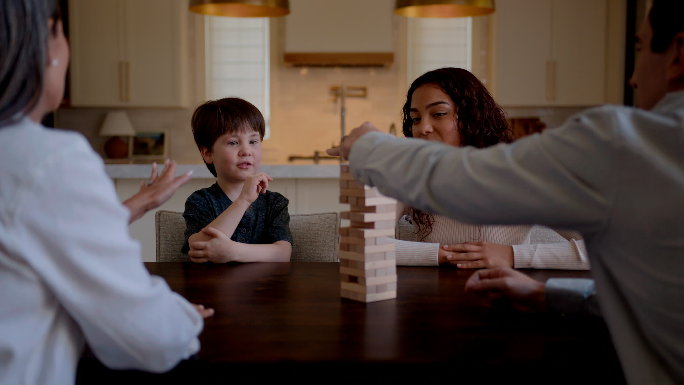 Warm kitchen table frame with a child playing Jenga between family members.